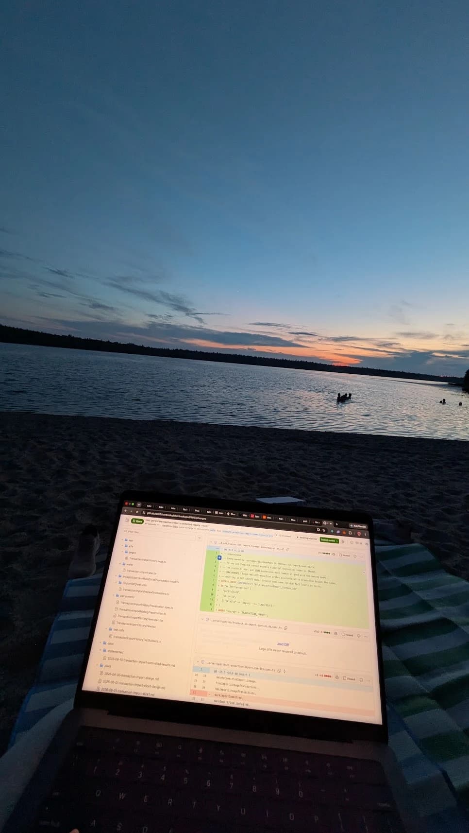 Laptop showing a code review, on a beach at sunset