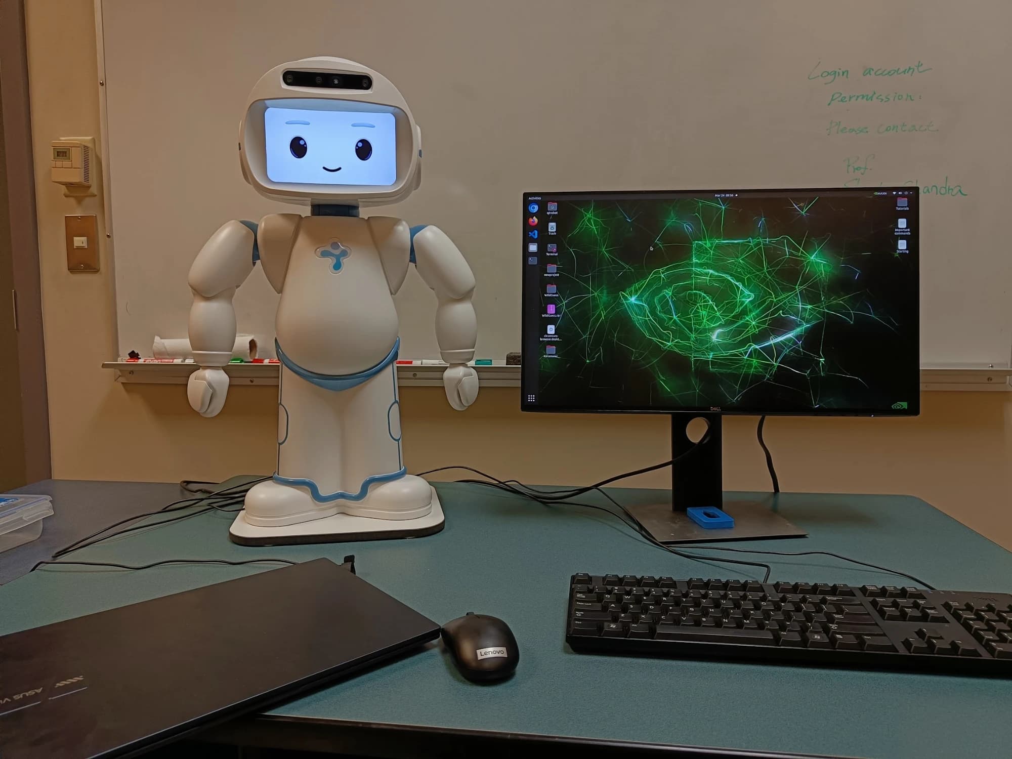 A small humanoid robot on a desk beside a monitor in a research lab